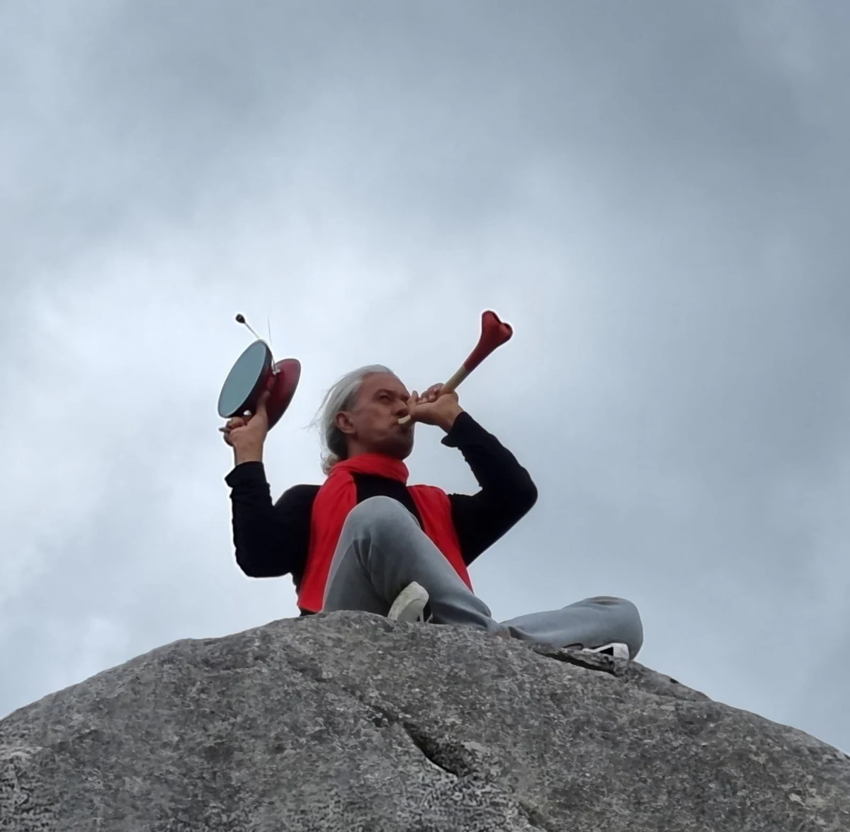 Paora seduto su una roccia a Castle Hill suona uno strumento a fiato sotto il cielo aperto.