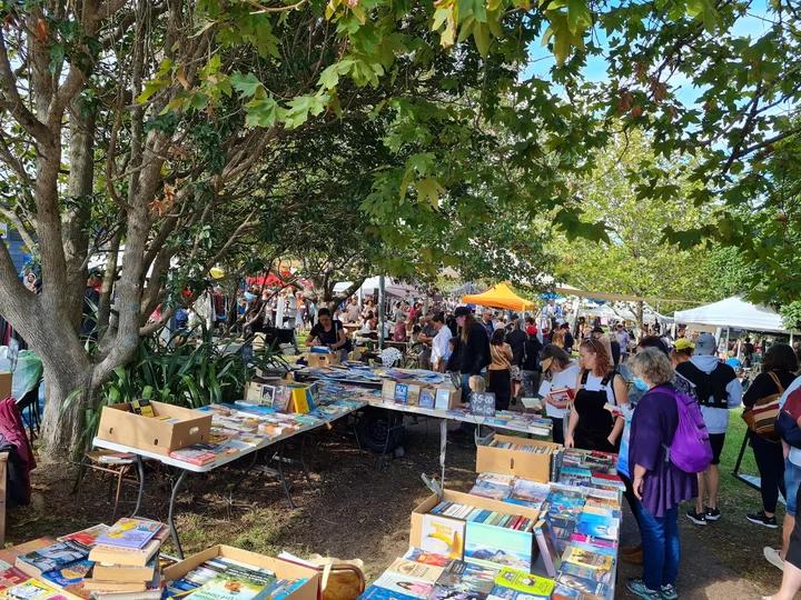 Tavoli di libri, bancarelle e visitatori sotto gli alberi frondosi di Ostend Market.
