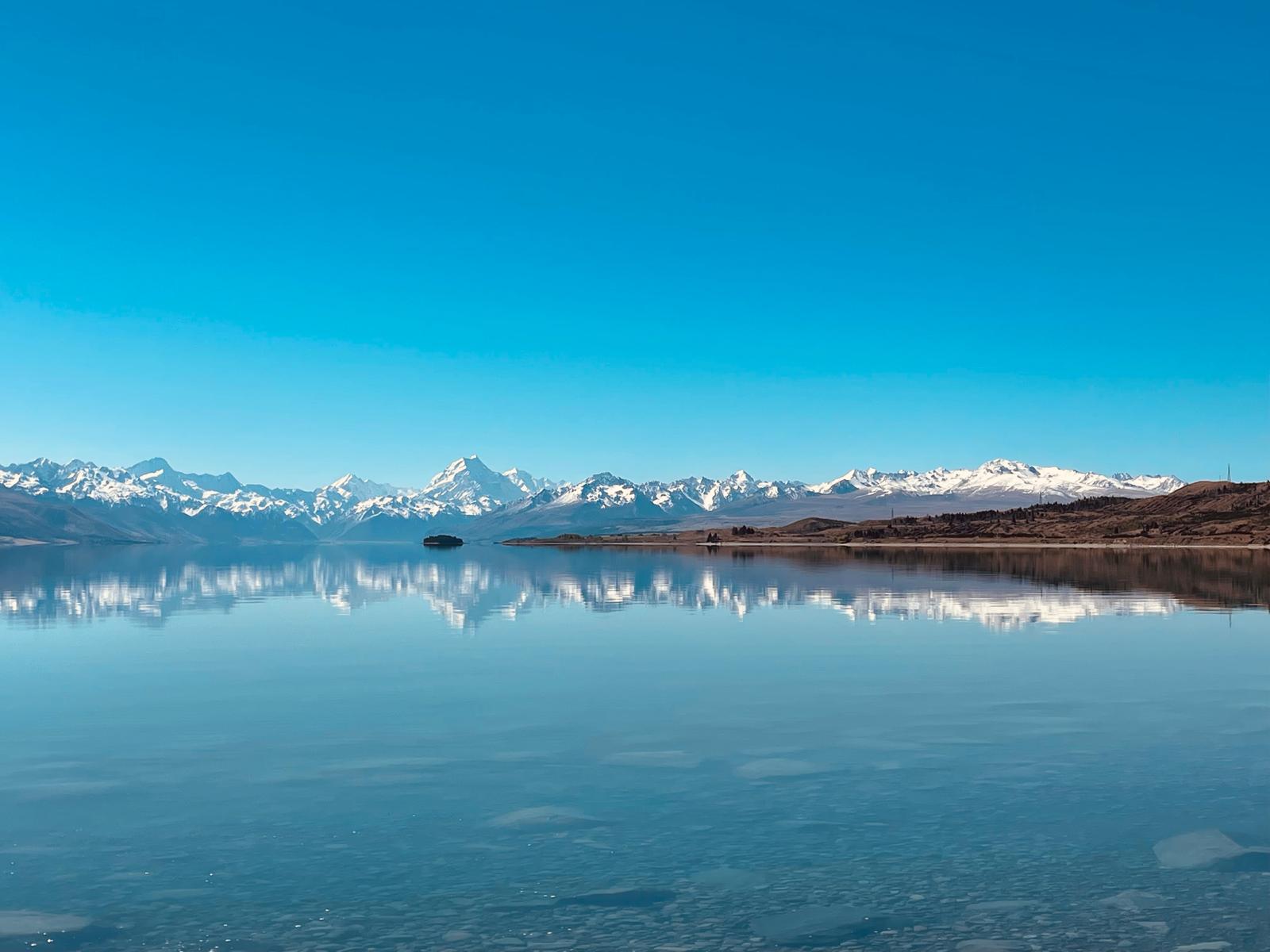 Snow-covered mountains reflected in still water beneath a clear blue sky.