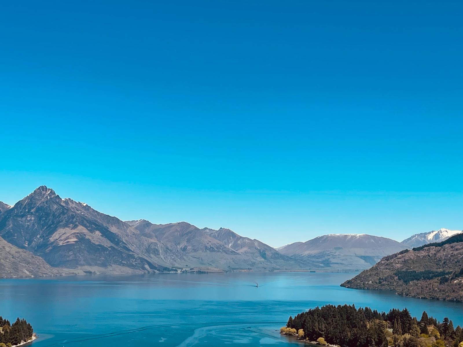 A mountain range above a deep-blue lake, with wooded shoreline in the foreground.