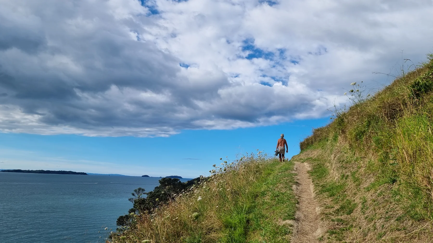 Eine kleine Gestalt auf einer Landzunge von Waiheke unter weitem Himmel.