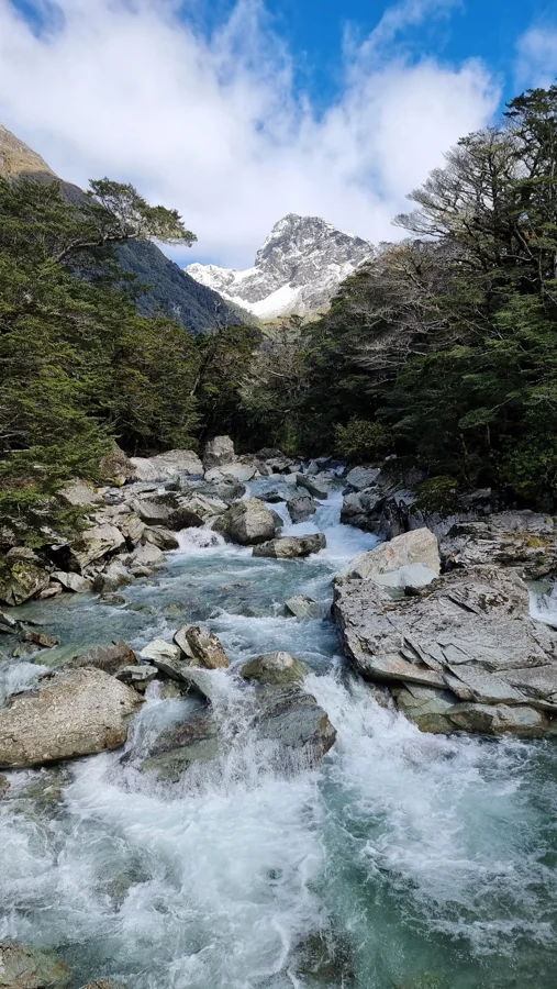An alpine river flowing between rocks beneath a snow-covered mountain.